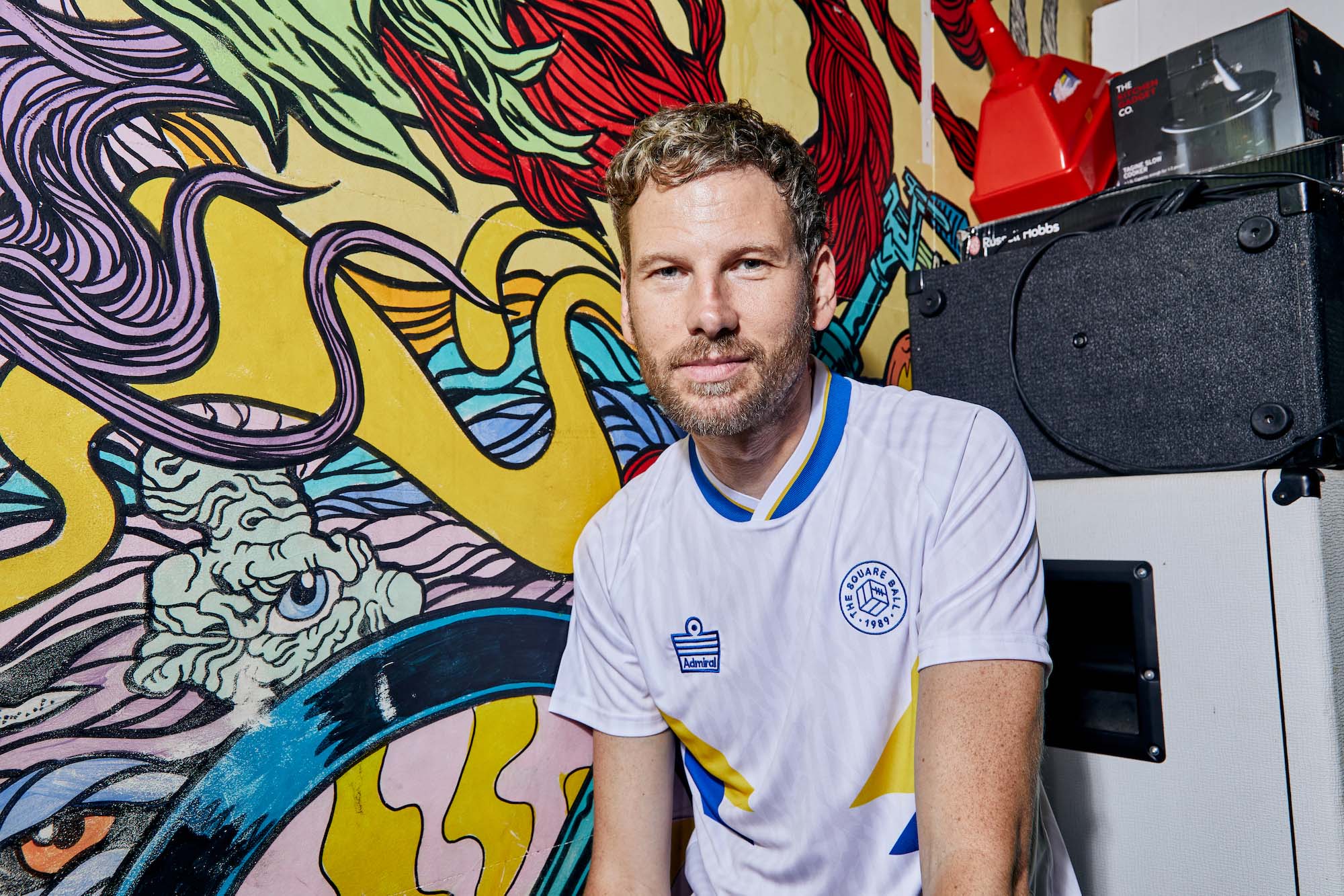 Kaiser Chiefs bassist Simon Rix models a 2022 shirt in the colours of a Leeds United home shirt, made for The Square Ball by Admiral.