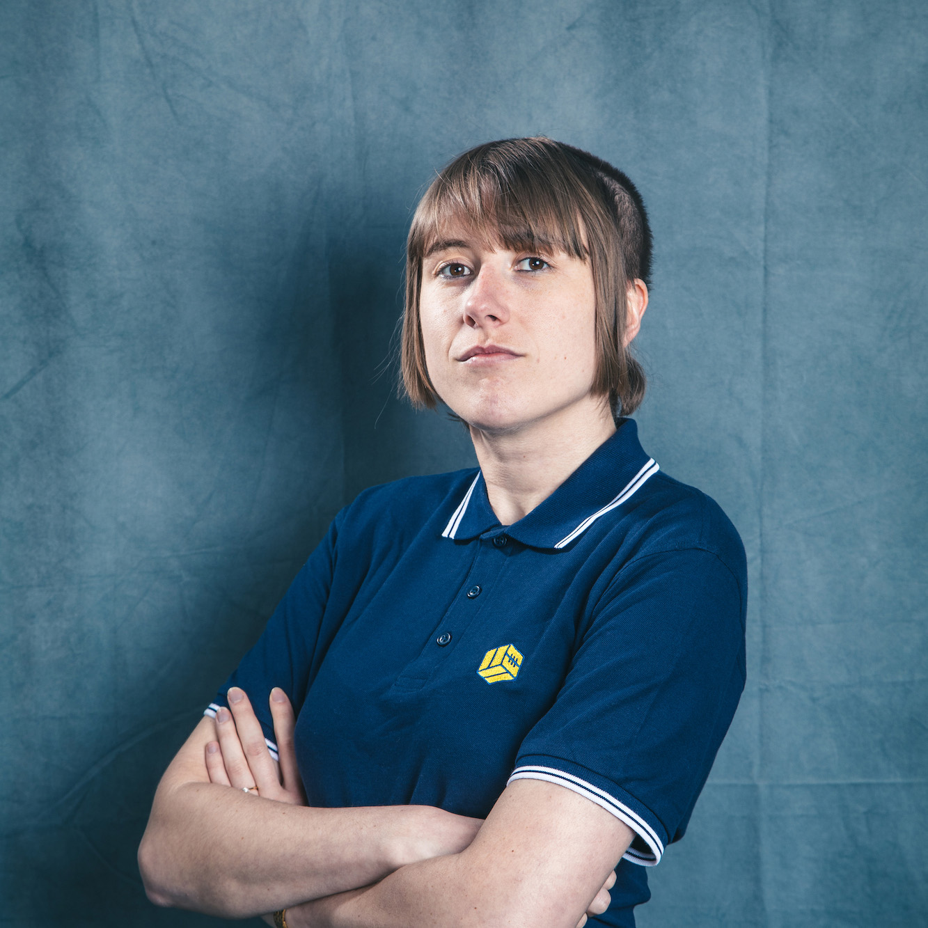 Comedian Maisie Adam models a navy polo shirt featuring the central ball icon of The Square Ball logo.