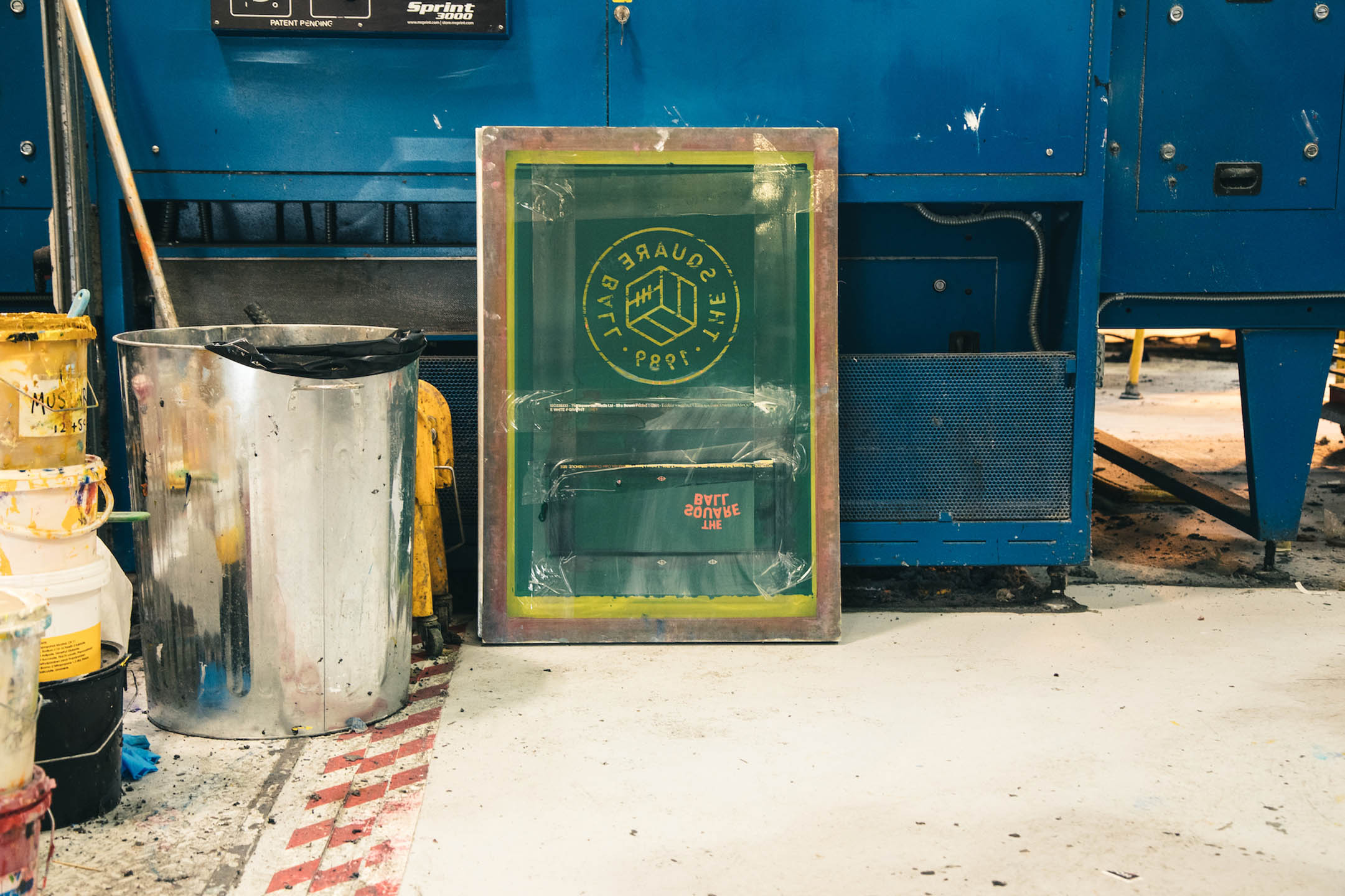 The Square Ball logo is seen on a screenprinting frame, propped up on the floor of a printer's shop.