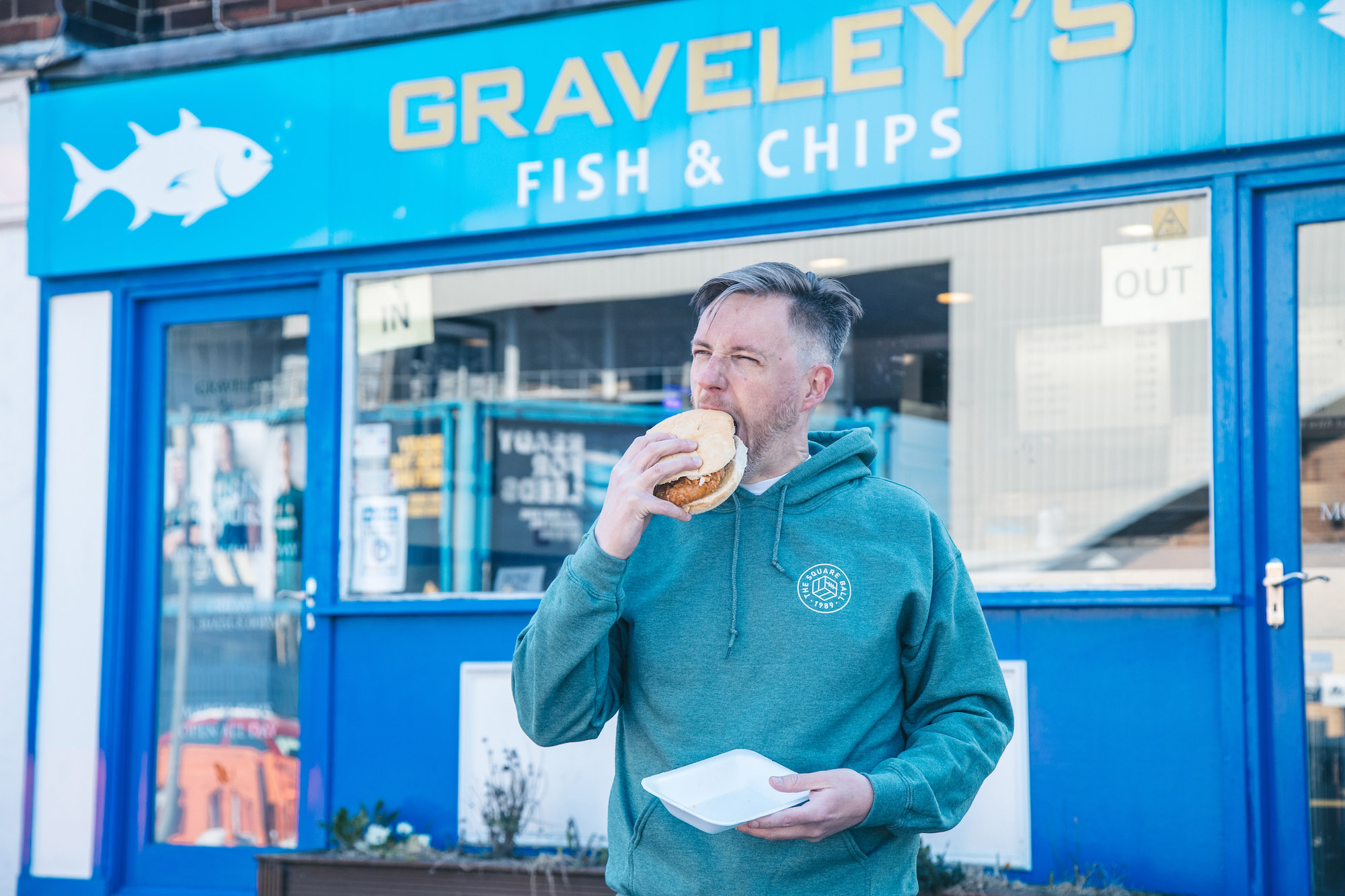 A fan outside Graveley's fish and chip shop wears a hoodie featuring the logo of The Square Ball.